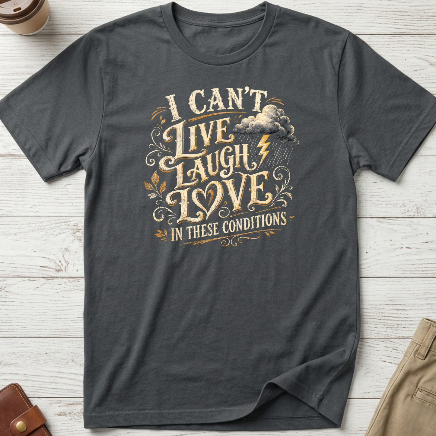 I Can’t Live Laugh Love In These Conditions funny sarcastic t-shirt featuring vintage cream lettering with storm cloud and lightning graphic on a grey unisex tee.