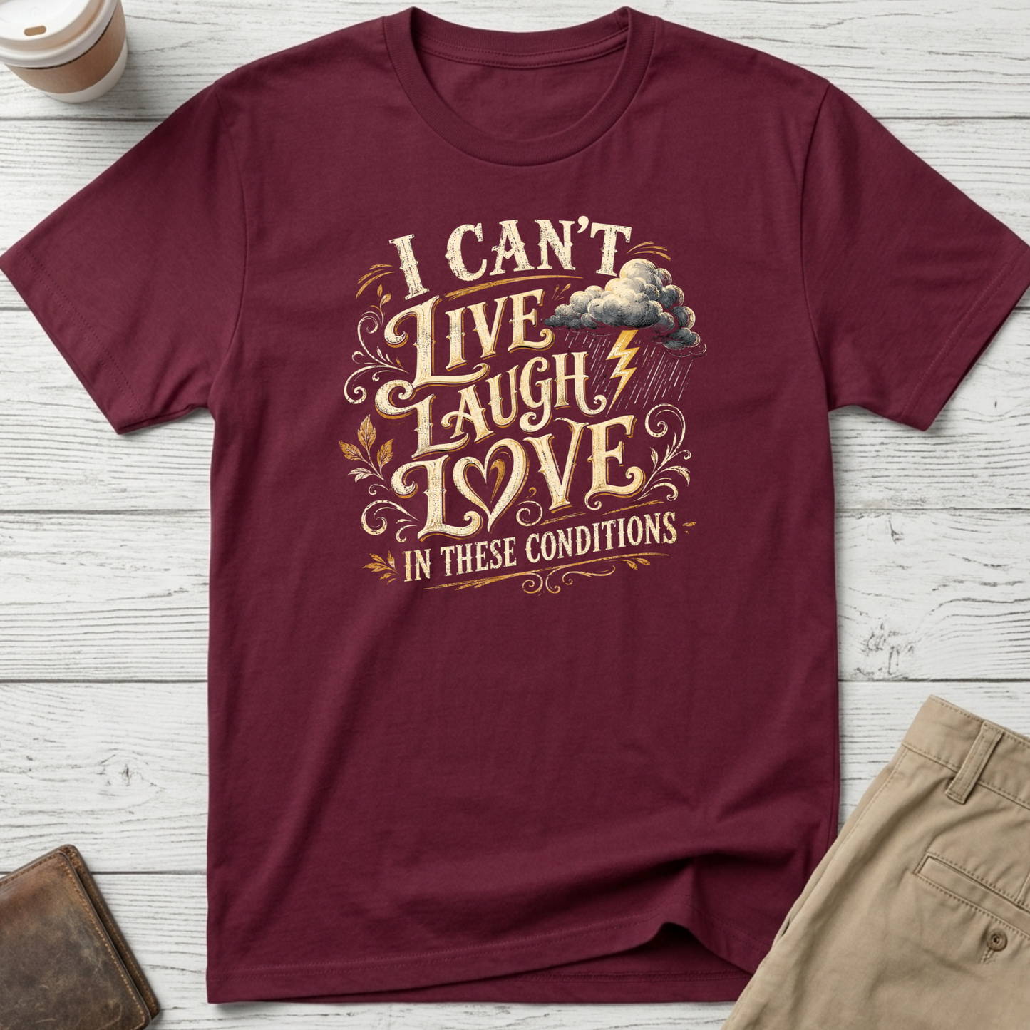 I Can’t Live Laugh Love In These Conditions funny sarcastic t-shirt featuring vintage cream lettering with storm cloud and lightning graphic on a maroon unisex tee.
