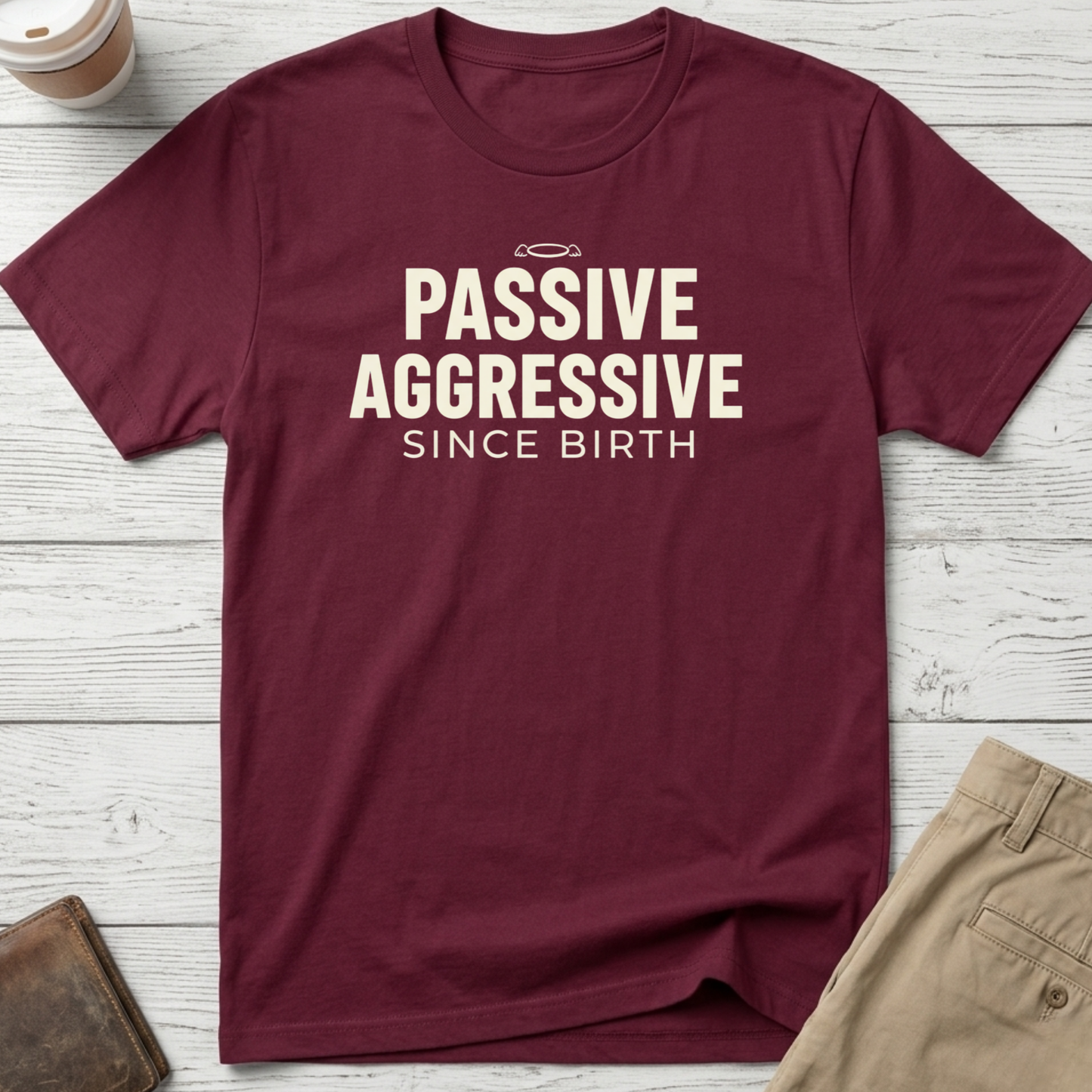 Passive Aggressive Since Birth funny sarcastic t-shirt featuring bold cream text and small halo graphic on a maroon unisex tee.